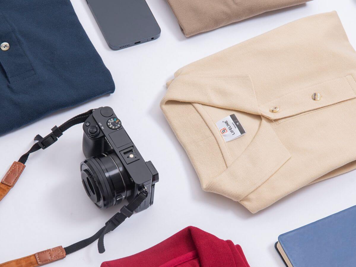 Flat lay of polo shirts in different sizes alongside a camera and mobile phone, representing versatile on-the-go lifestyle wear.