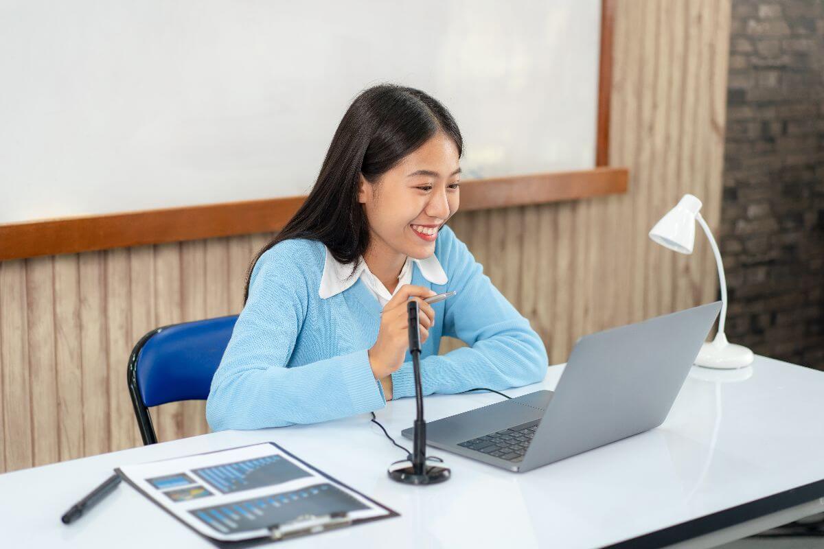 Smiling woman speaks into a desktop microphone while using a laptop, illustrating virtual assistant communication and remote meeting support.
