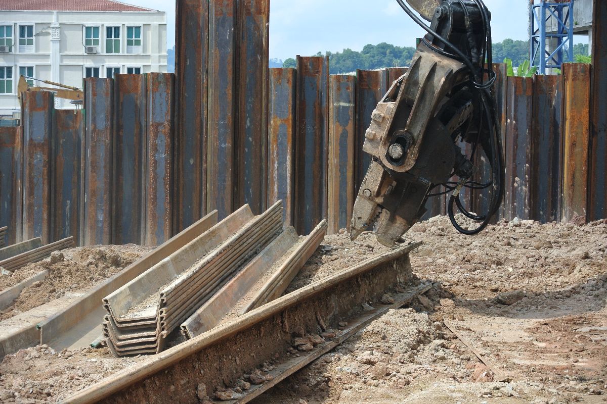 Excavator driving steel sheet piles into the ground for marine or infrastructure construction