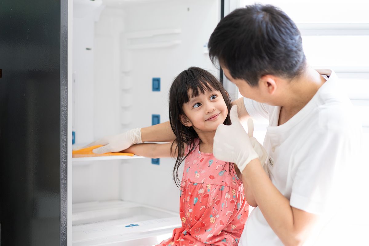 Father and daughter cleaning the interior of a refrigerator together while wearing protective gloves