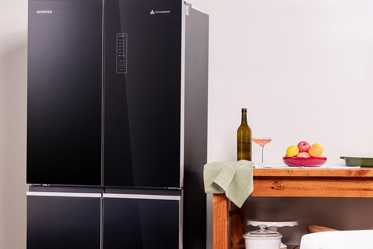 Black four-door inverter refrigerator displayed beside a wooden kitchen table with fruit and dining items