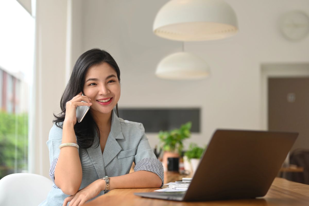 Virtual assistant speaking with a client on the phone while working on a laptop from a home office.