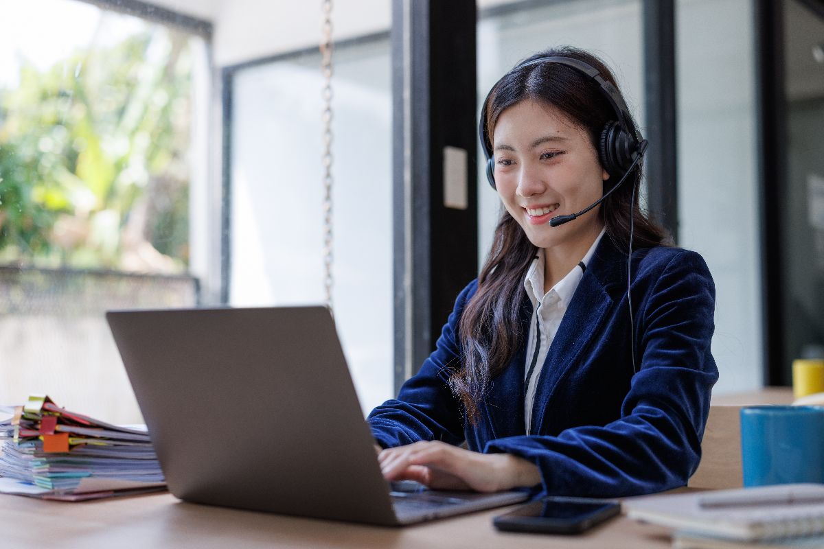Filipina virtual assistant wearing a headset while working on a laptop in a bright office