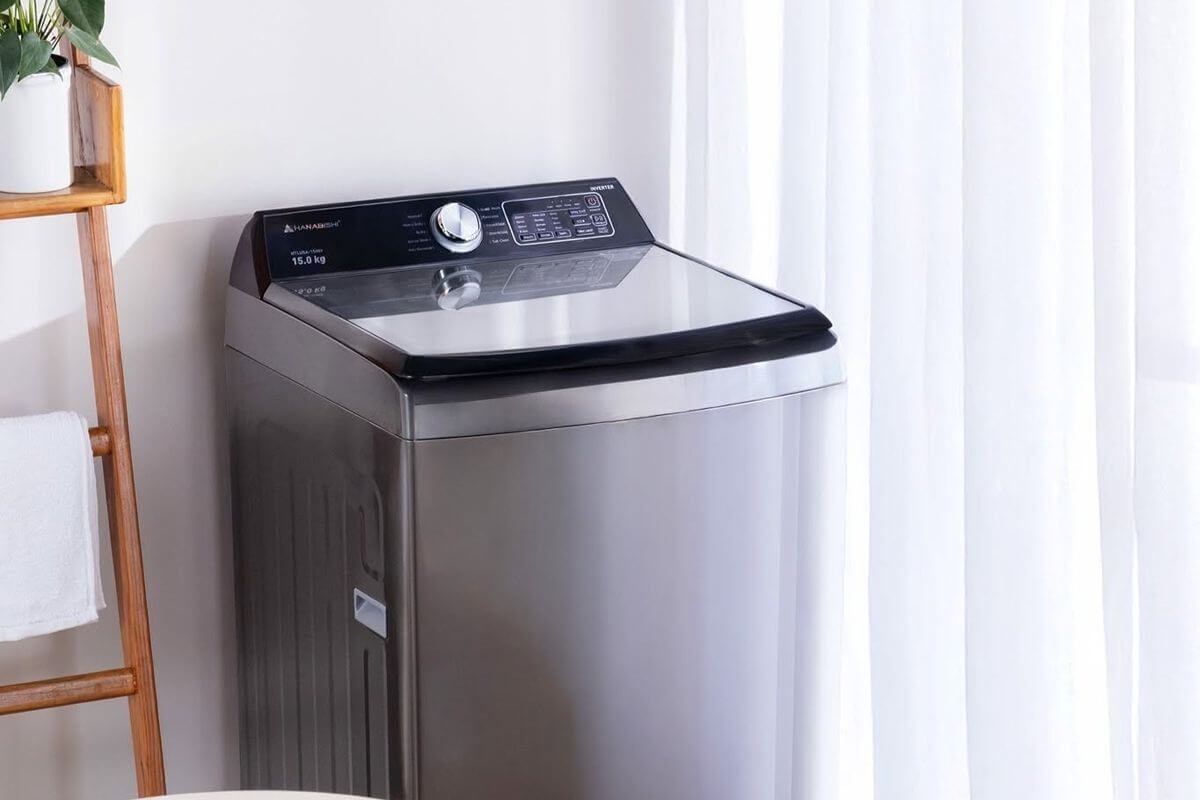 Compact top-load washing machine placed in a small condo laundry space beside a window