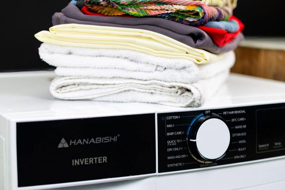 Folded clothes stacked on top of a Hanabishi inverter front-load washing machine