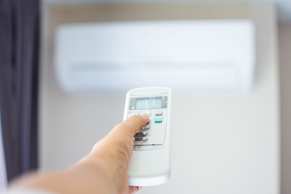 Close-up of a person using a remote control to operate an air conditioner inside an apartment