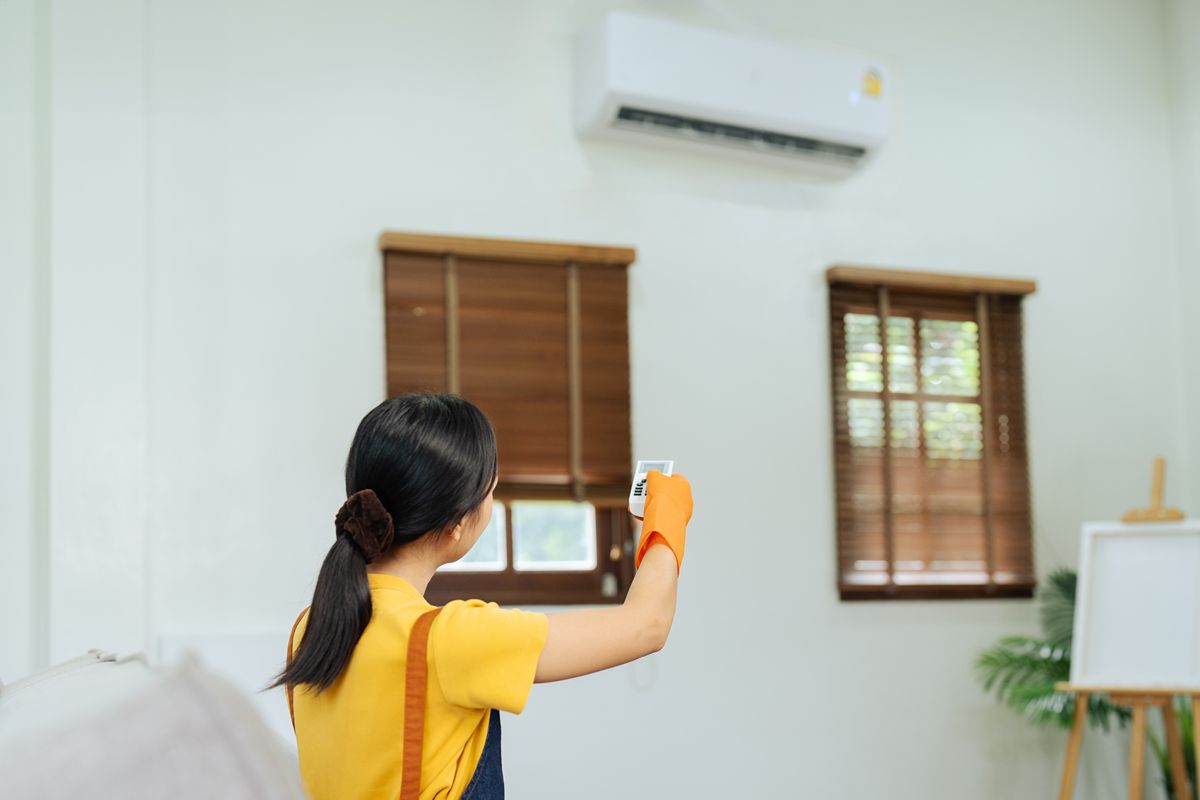 Woman using a remote control to adjust a wall-mounted air conditioner in a compact apartment living space