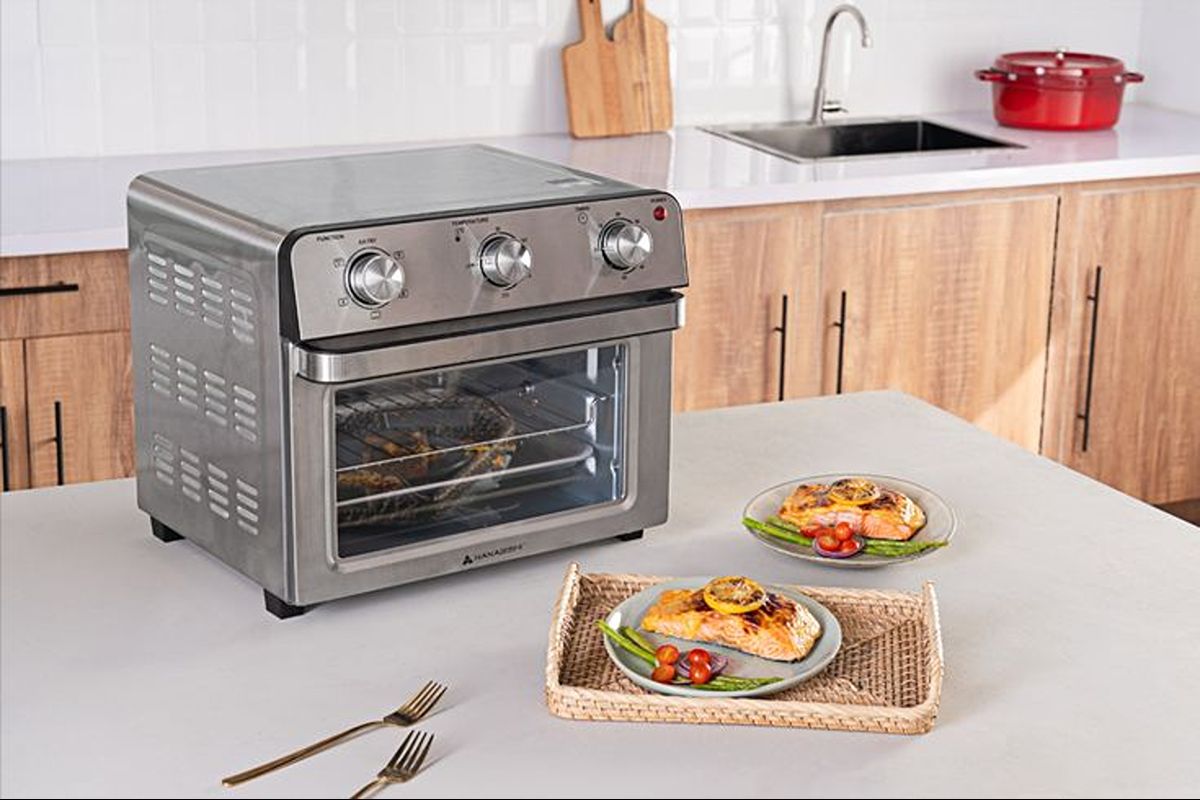 Stainless steel air fryer oven with plated food on a kitchen counter