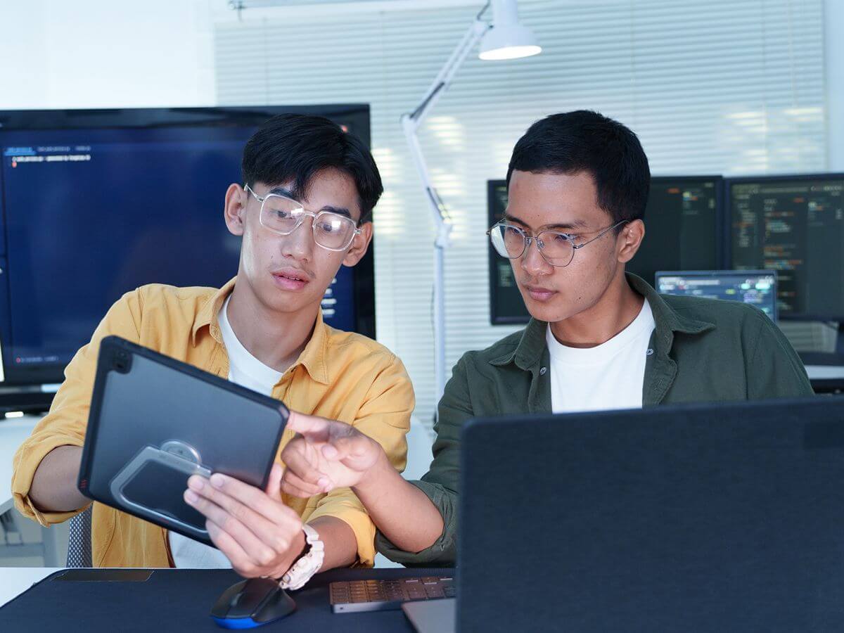 Two tech students review a digital project using a tablet and laptop in a computer laboratory