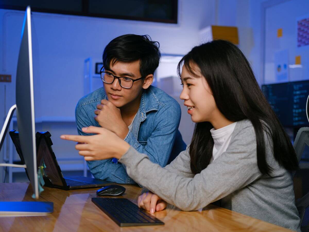 Two students practice programming together while reviewing their work on a desktop computer